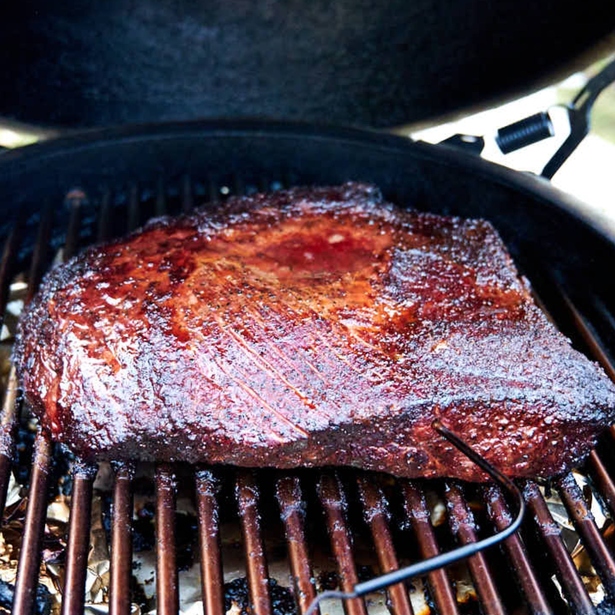 A premium USDA Prime Black Angus whole packer brisket smoking inside a Big Green Egg grill, displaying a deep mahogany bark and an inserted temperature probe, direct from Whole Cow.
