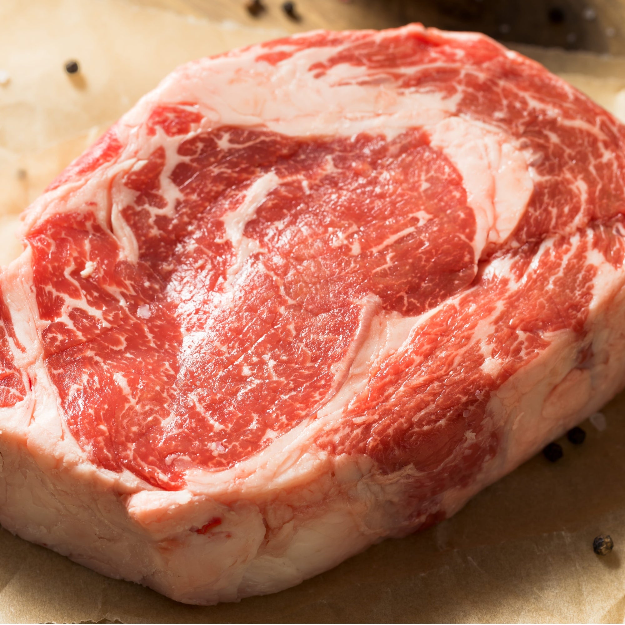 A raw, thickly cut boneless USDA Prime Black Angus ribeye steak displaying exceptional intramuscular fat marbling, custom-processed at Whole Cow.