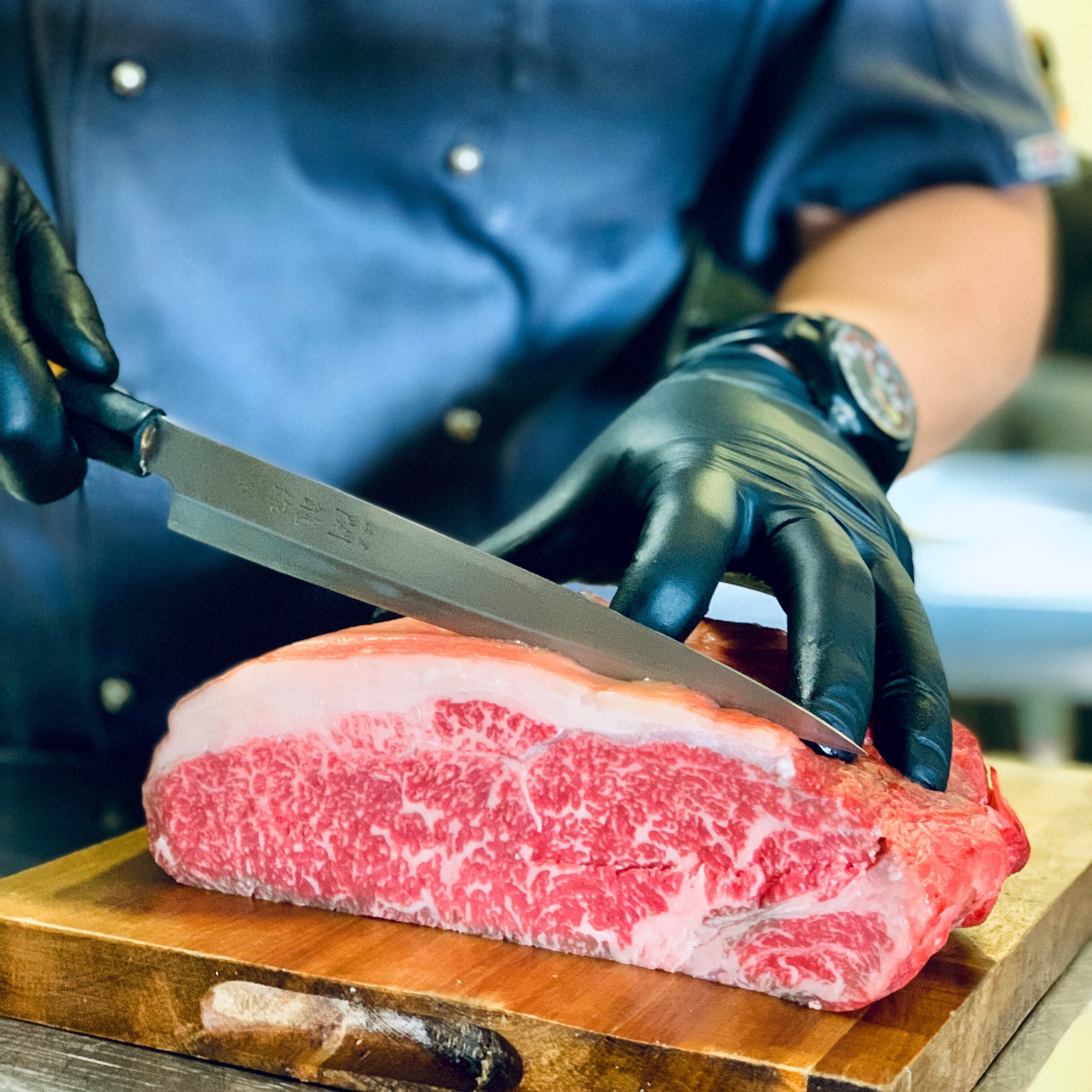 An artisan butcher slicing a heavily marbled raw 100% Fullblood American Wagyu New York strip loin on a wooden cutting board at Whole Cow's in-house custom processing plant.