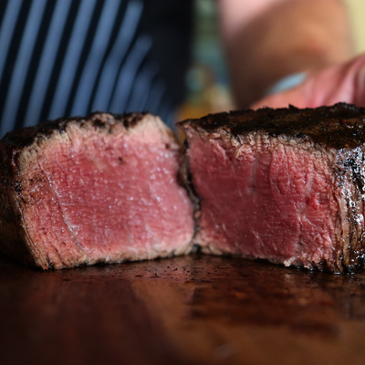 A perfectly grilled, medium-rare USDA Prime Black Angus filet mignon steak sliced open on a dark wood cutting board to show its juicy texture, direct from Whole Cow.