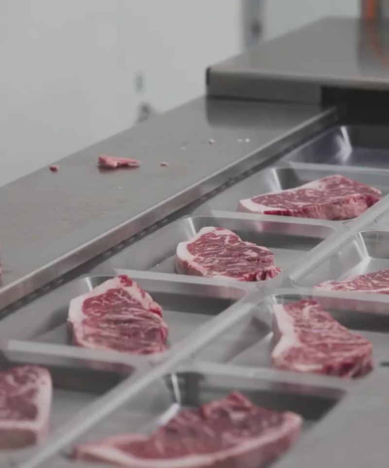 A close-up look inside the clean Whole Cow processing facility showing an automated cutting machine precisely slicing a premium whole loin into thick, uniform USDA Prime steaks.