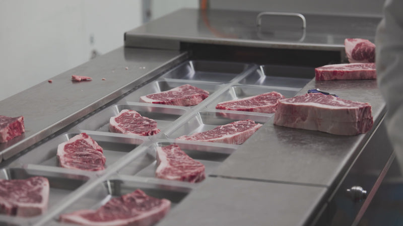 A close-up look inside the clean Whole Cow processing facility showing an automated cutting machine precisely slicing a premium whole loin into thick, uniform USDA Prime steaks.