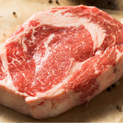 A raw, thickly cut boneless USDA Prime Black Angus ribeye steak displaying exceptional intramuscular fat marbling, custom-processed at Whole Cow.